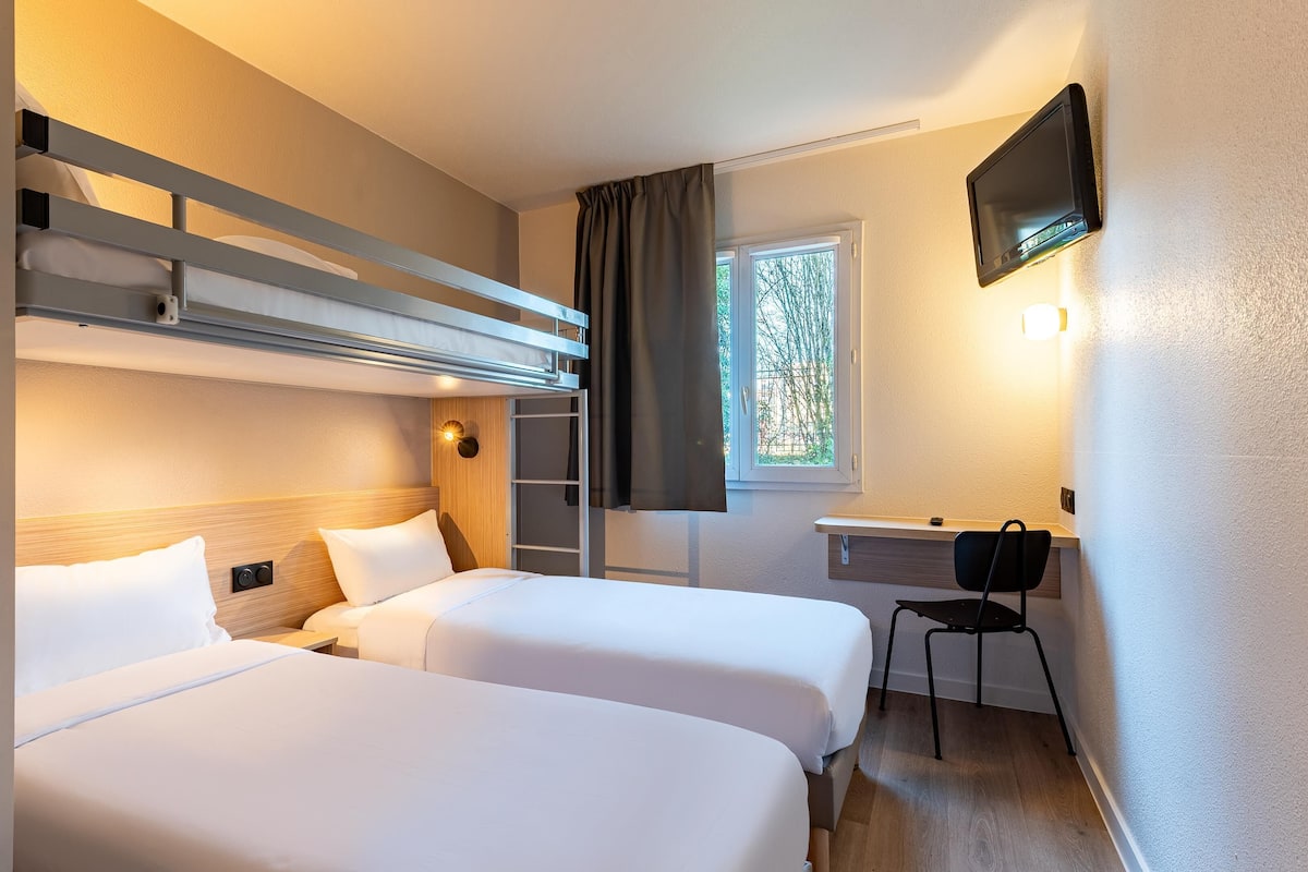 Camera d'albergo con due letti, una scrivania, una sedia, una televisione e una finestra con tende.