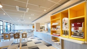 A modern cafeteria with a checkered floor, seating area, and a coffee station with branded machines. - Kyriad ECO - Marne-la-Vallée Bussy-Saint-Georges (Bussy-Saint-Georges)