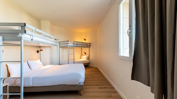 A hotel room with bunk beds, a wooden floor, a window with curtains, and a wall-mounted lamp. - Kyriad ECO - Marne-la-Vallée Bussy-Saint-Georges (Bussy-Saint-Georges)