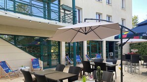 An outdoor patio area with wicker furniture, tables, and chairs, some with umbrellas. - Kyriad ECO - Marne-la-Vallée Bussy-Saint-Georges (Bussy-Saint-Georges)