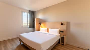 A modern hotel room with a large bed, a bedside table, a nightstand, and a window with curtains.