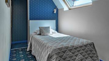 A bedroom with a sloped ceiling, a skylight, a patterned carpet, and a bed with a geometric-patterned bedspread.