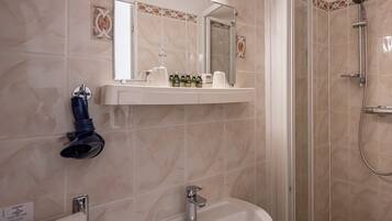 A bathroom with a sink, mirror, shower, and a shelf with toiletries.