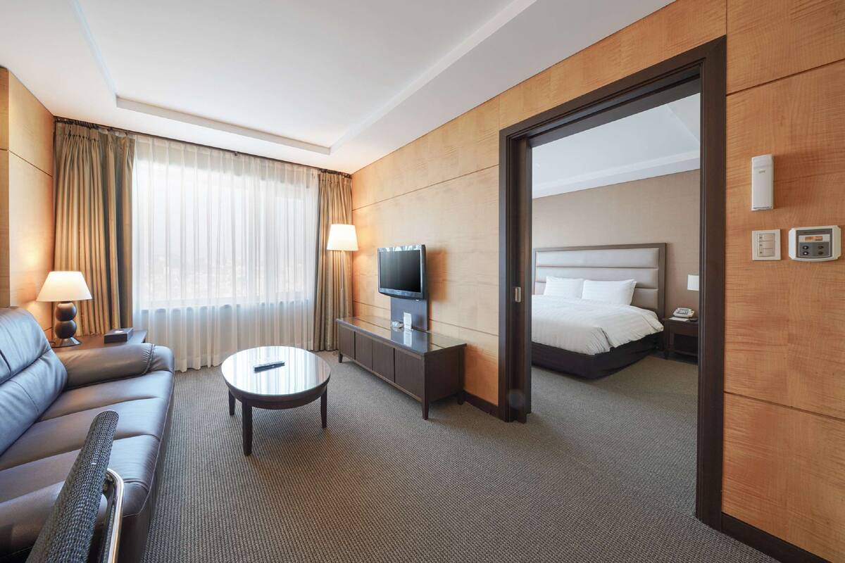 Een hotelkamer met een bank, een salontafel, een televisie, een bed en een deur naar een andere kamer.