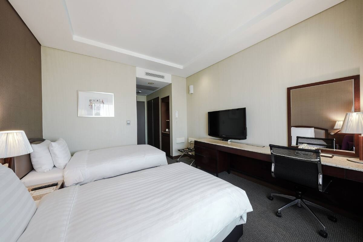 Een hotelkamer met twee bedden, een bureau met een computer, een televisie en een spiegel.