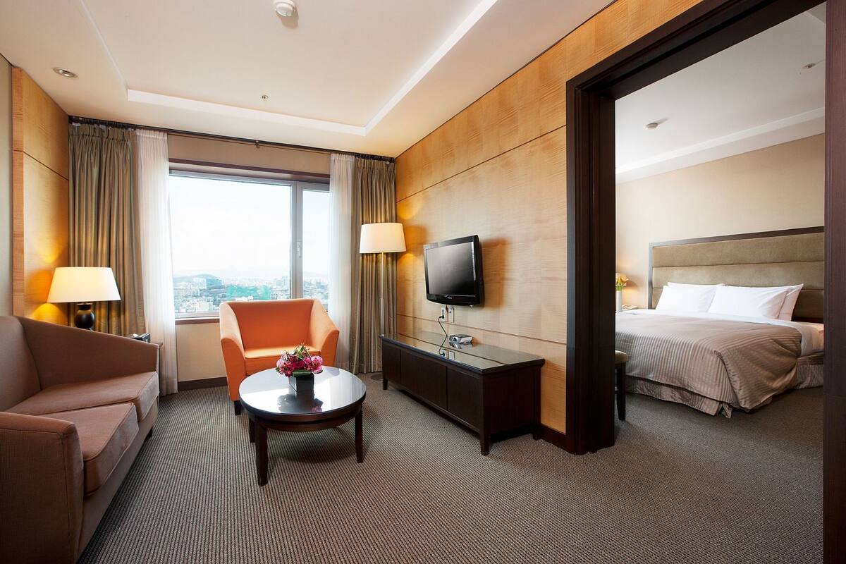 Een hotelkamer met een slaapbank, fauteuil, televisie, nachtkastje en een bed.