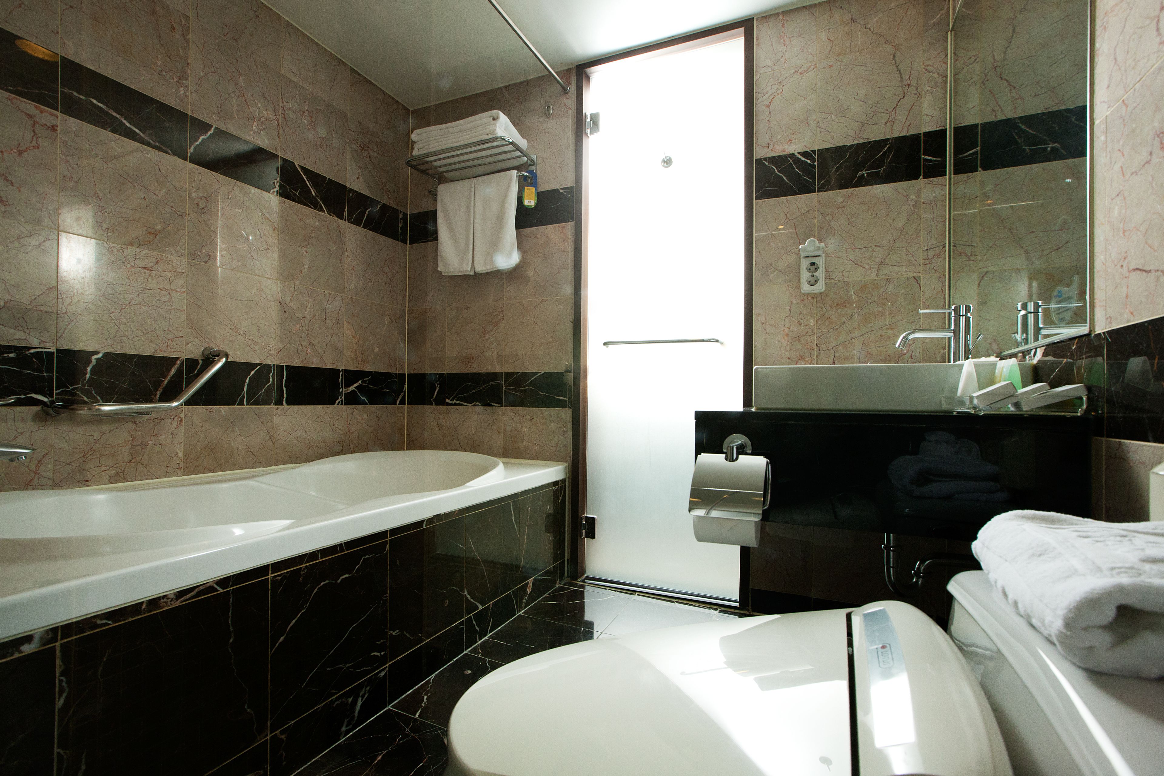 A modern bathroom with a bathtub, toilet, and a large mirror.