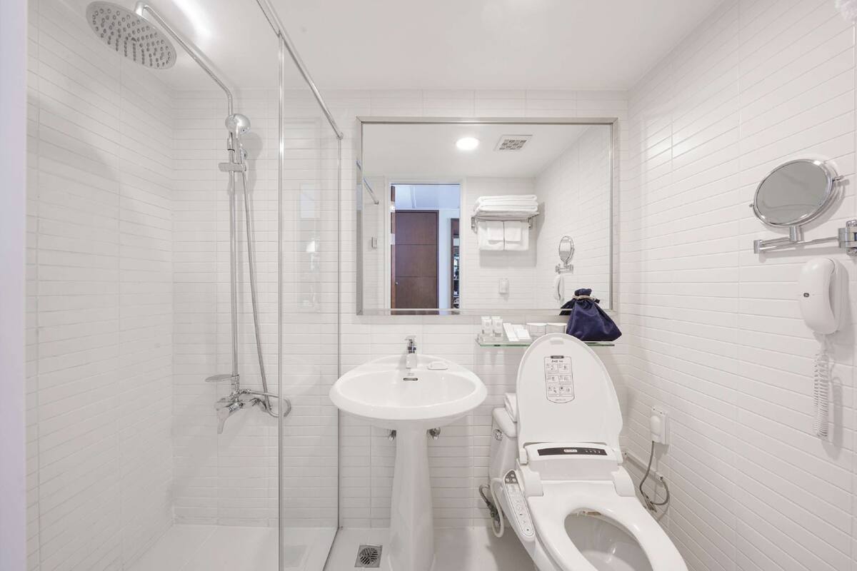 Een moderne badkamer met een douchecabine van glas, een witte wastafel en een toilet met bedieningspaneel.
