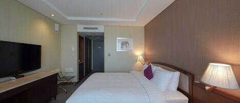Habitación de hotel con una cama grande, un televisor en un escritorio, una lámpara y un teléfono en la mesita de noche.
