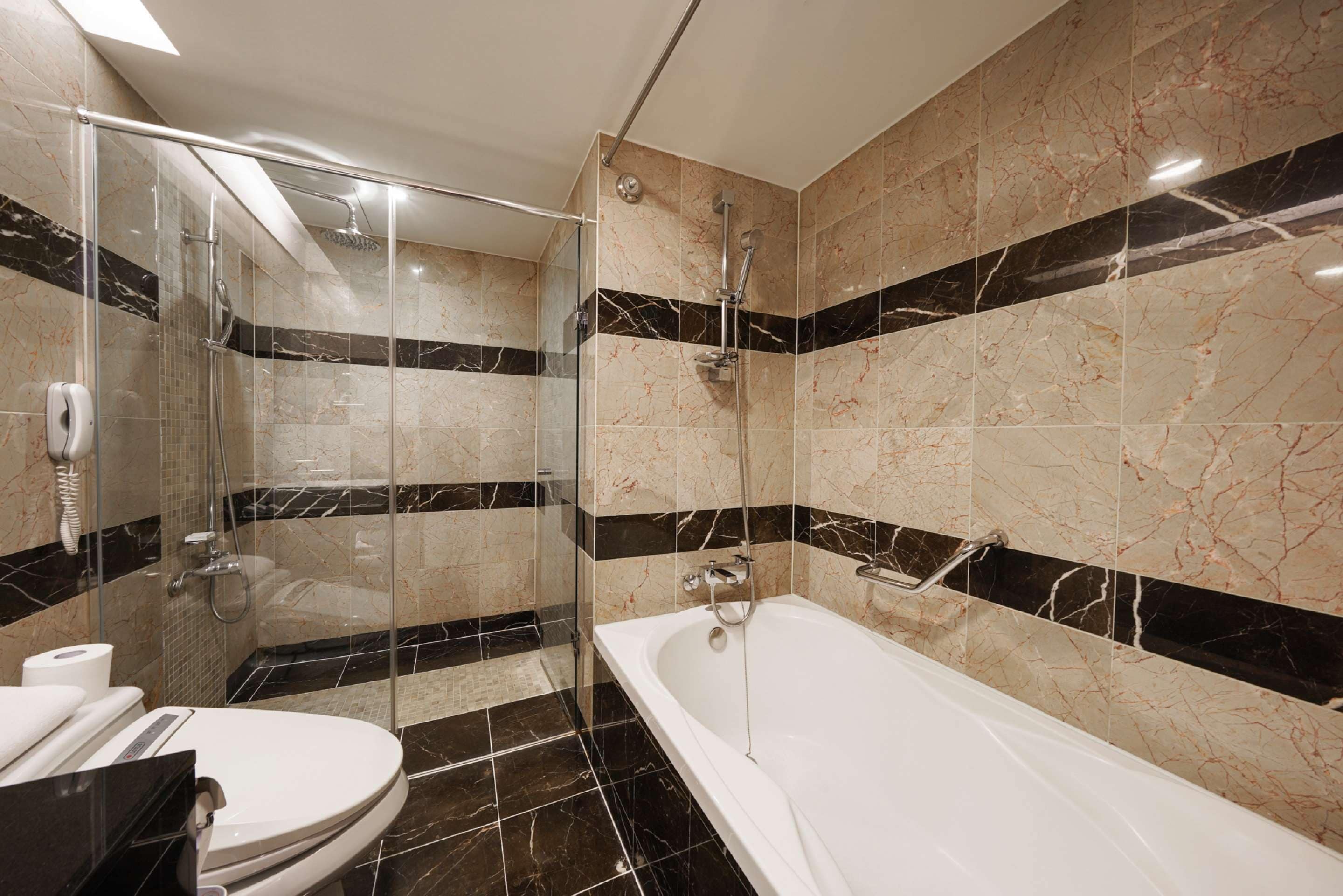 Un baño moderno con ducha de vidrio, una bañera blanca y azulejos de mármol negros y beige.