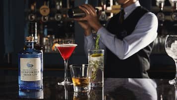 A bar setting with a bottle of Drumshanbo Gunpowder Irish Gin, a red cocktail, and a glass with a mint sprig.