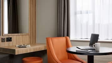 Habitación de hotel moderna con un escritorio de madera, una silla de cuero, una mesa redonda con una computadora portátil y una taza, y un espejo grande en la pared.