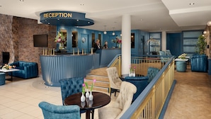 A reception area with a blue theme, including a reception desk, seating, and a staircase. - Springfield Hotel (Leixlip)
