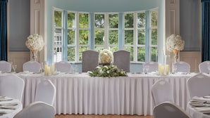 A formal dining room with a bay window, white tablecloths, and floral centerpieces. - Springfield Hotel (Leixlip)