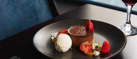 Un plato de postre con mousse de chocolate, una bola de helado y fresas sobre un plato oscuro.