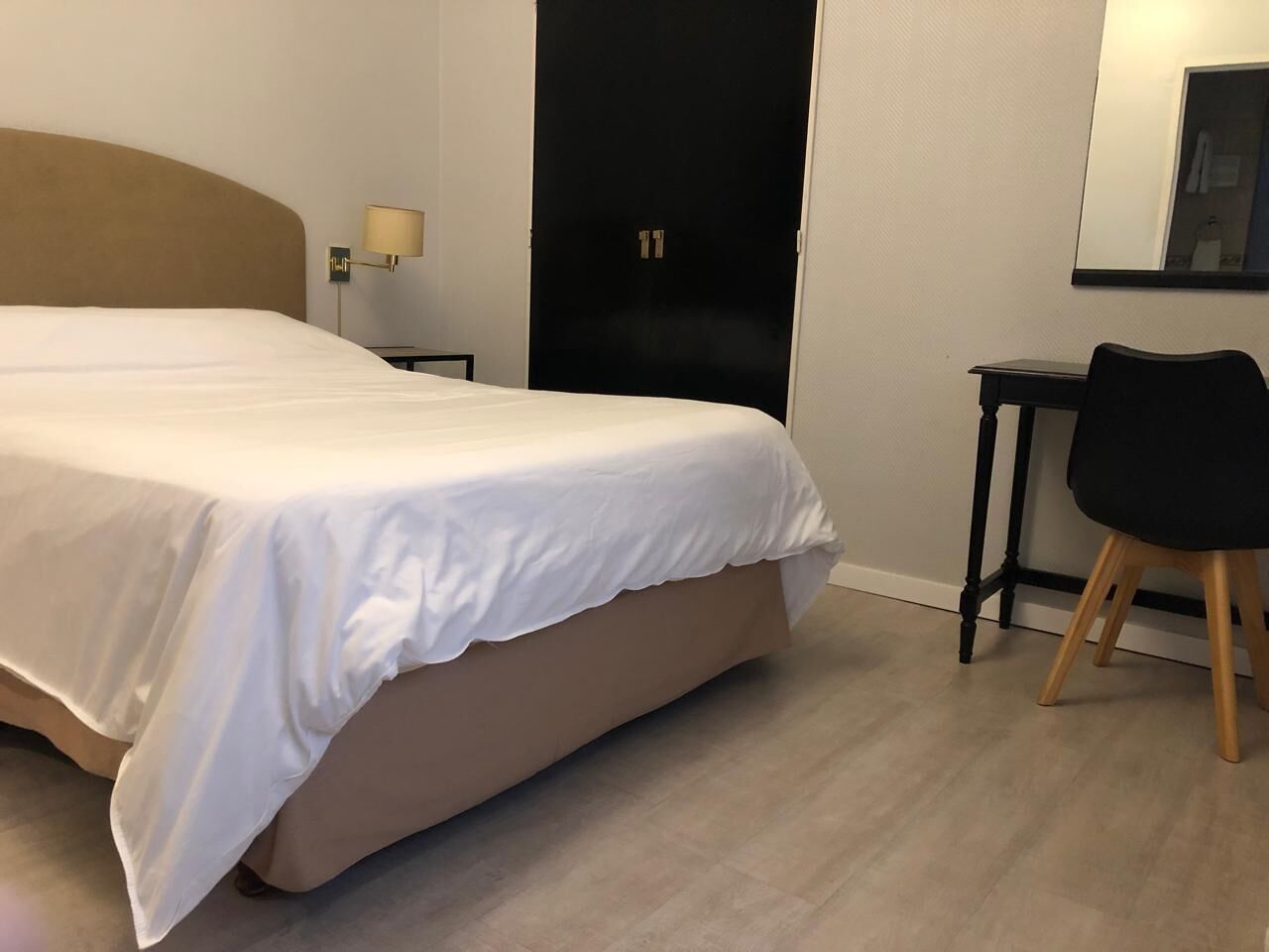 Habitación de hotel con una cama grande, un escritorio, una silla, una lámpara y una puerta.