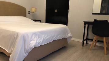 Habitación de hotel con una cama grande, un escritorio, una silla, una lámpara y una puerta.