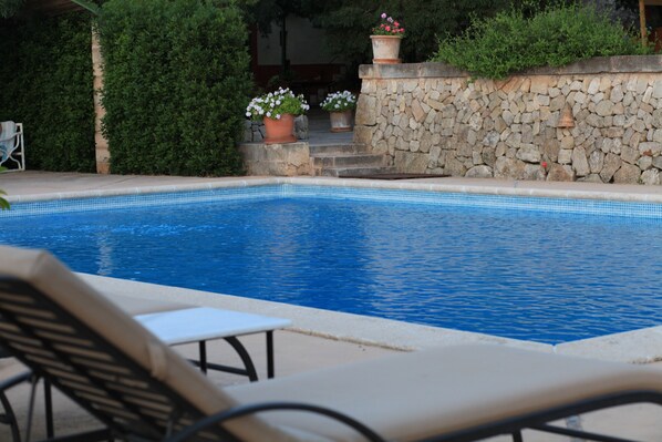 A swimming pool with a stone wall and potted plants.