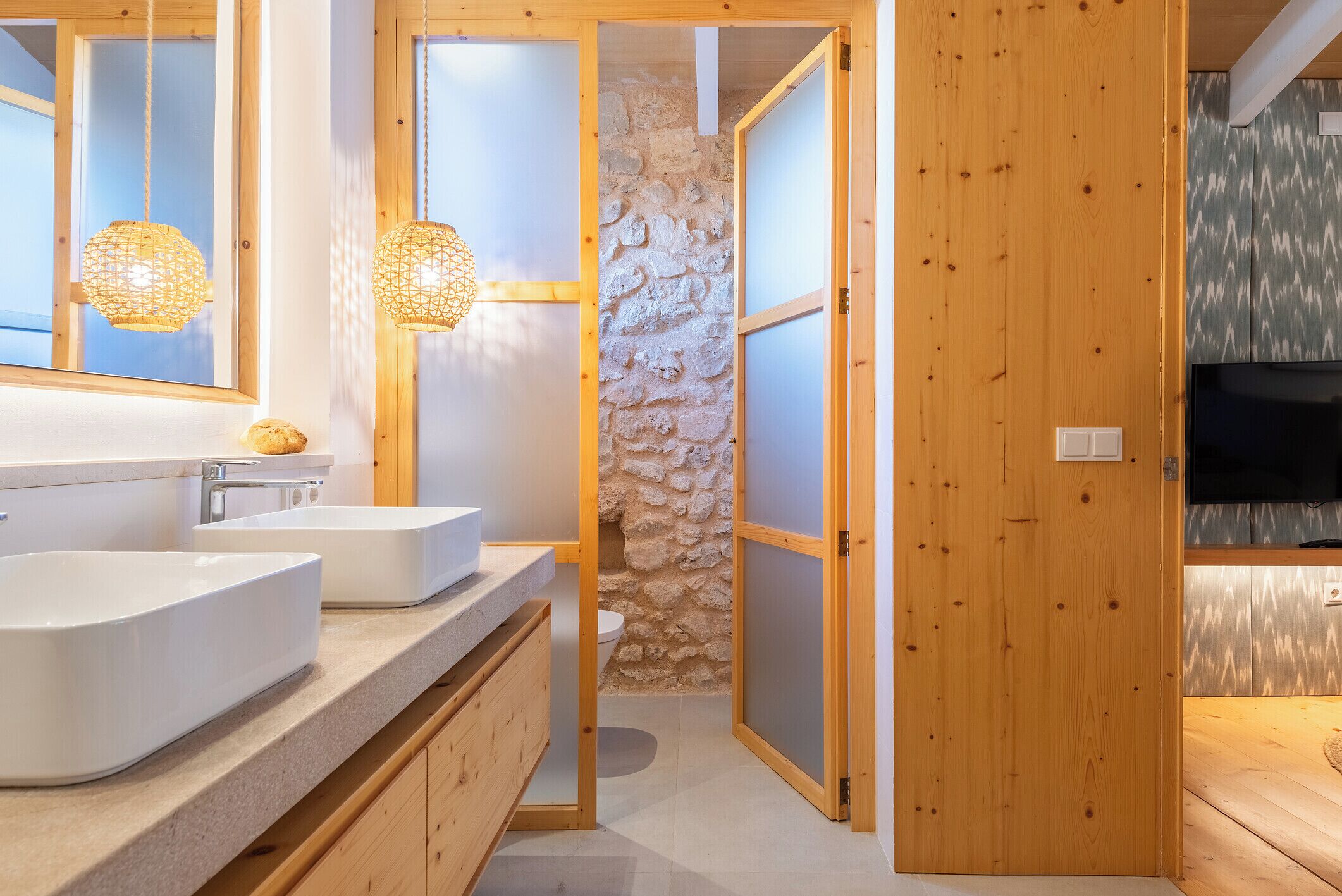 A modern bathroom with a wooden vanity, two sinks, and a stone wall.