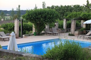 A pool with lounge chairs and a pergola in a landscaped outdoor area.