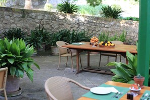 An outdoor patio with a wooden table set for dining, surrounded by potted plants and a stone wall.