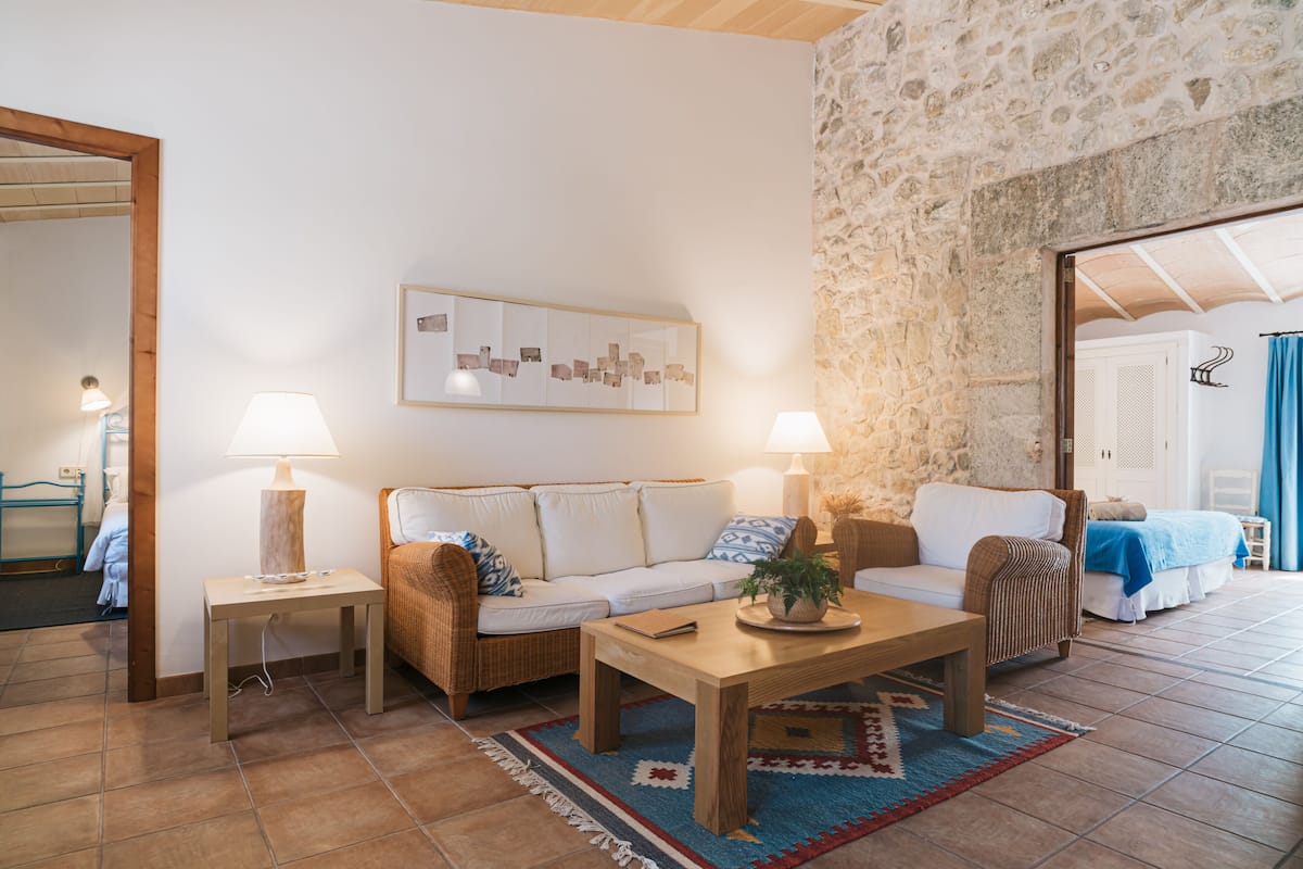 A cozy living room with a stone wall, a wooden ceiling, a sofa, a coffee table, and a lamp.