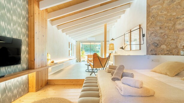 A modern hotel room with a wooden ceiling, a stone wall, a bed with towels, a TV, and a view of the outdoors. - Agroturismo sa Rota den Palerm (Lloret de Vistalegre)
