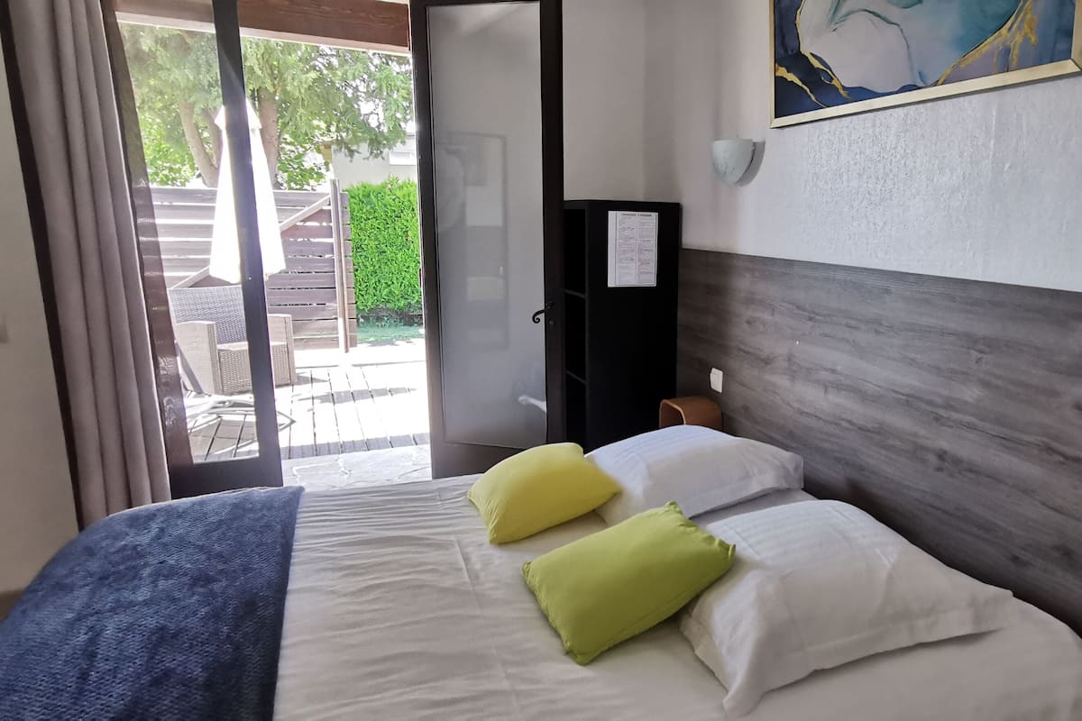 A bedroom with a bed, a wooden headboard, a nightstand, a wall-mounted lamp, and a painting.