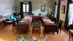 A conference room with a long table, chairs, and a small table with a vase of flowers. - Le Mas des Amandiers (Graveson)