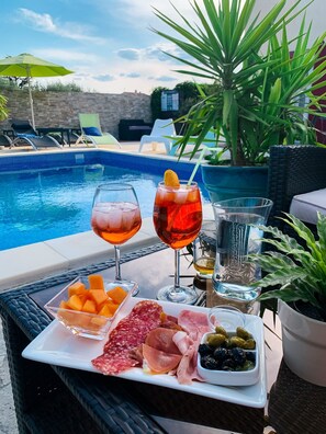 Ein Tisch am Pool mit Getränken, Obst und Wurstwaren.