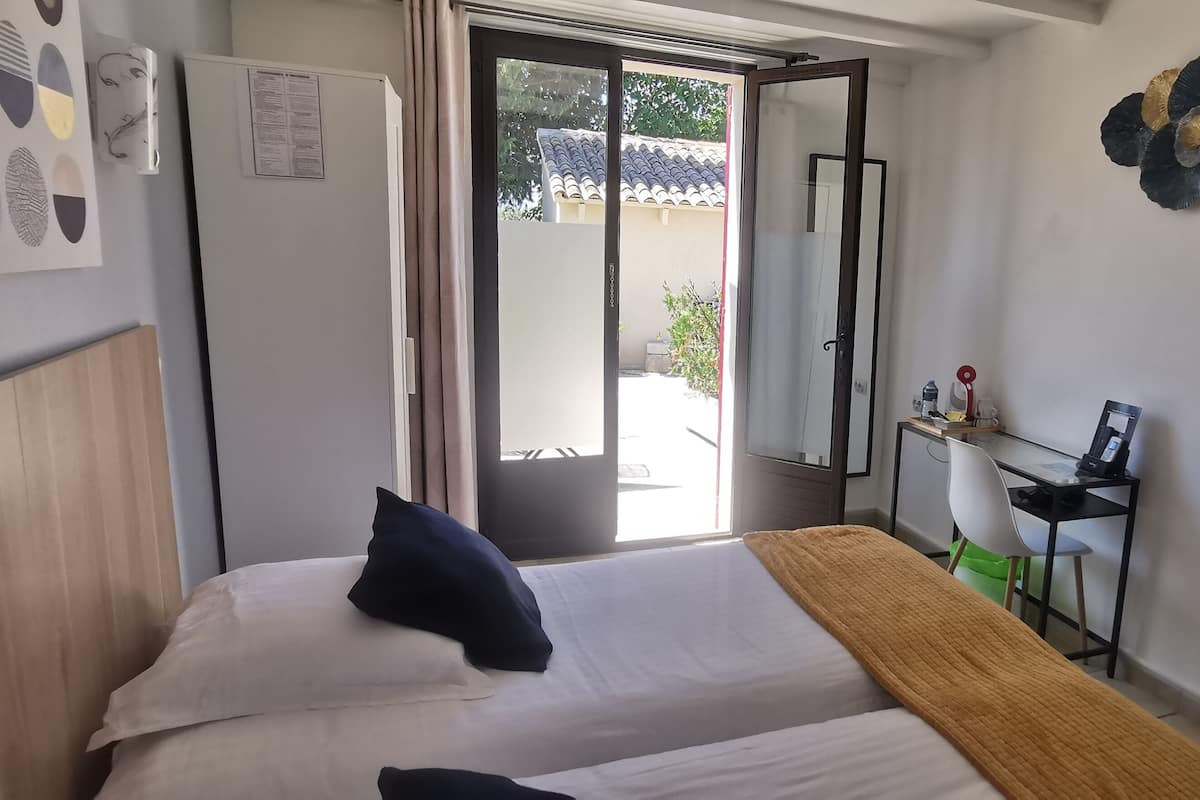 A bedroom with a bed, a desk, and a chair. There is a window with a view of the outside.
