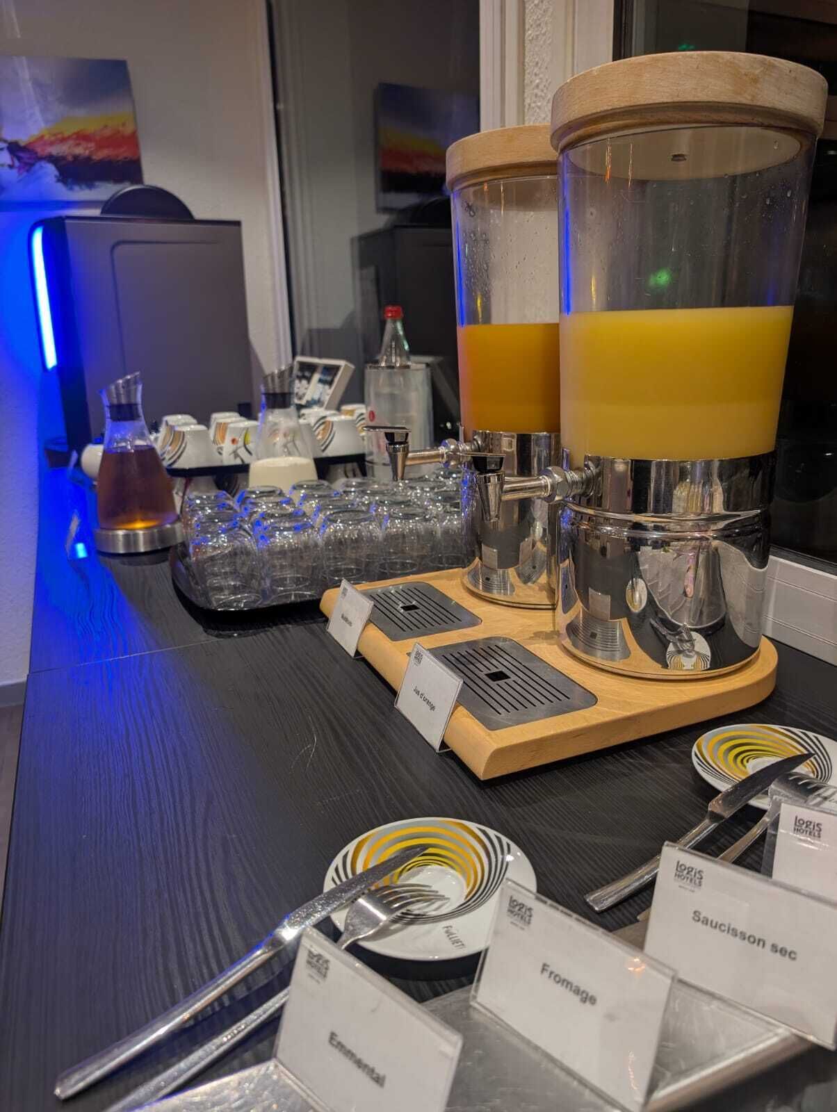 Zona de bar con dos grandes dispensadores de zumo, una selección de vasos y un atril con etiquetas de los productos.