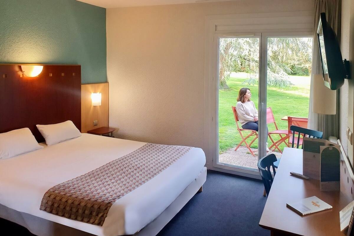 Hotelkamer met een bed, bureau, stoel, televisie en een schuifdeur naar een buitenruimte.