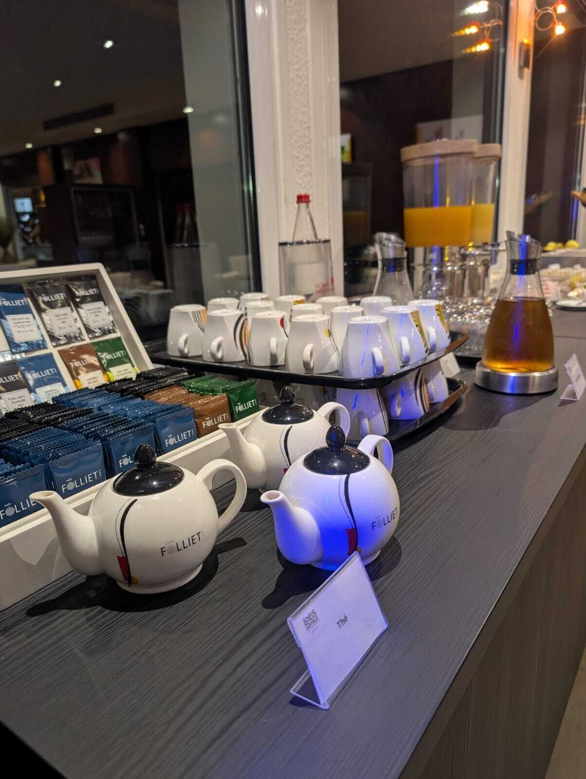 Une collection de théières et de tasses à thé est exposée sur un comptoir, accompagnée d’une enseigne indiquant la marque.