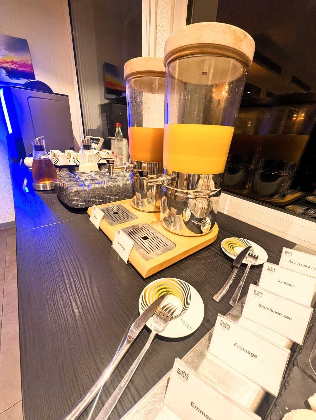 Zona de bar con dos grandes dispensadores, una variedad de vasos y un menú que incluye opciones como 'Saucisson à l'a' y 'Jambon'.