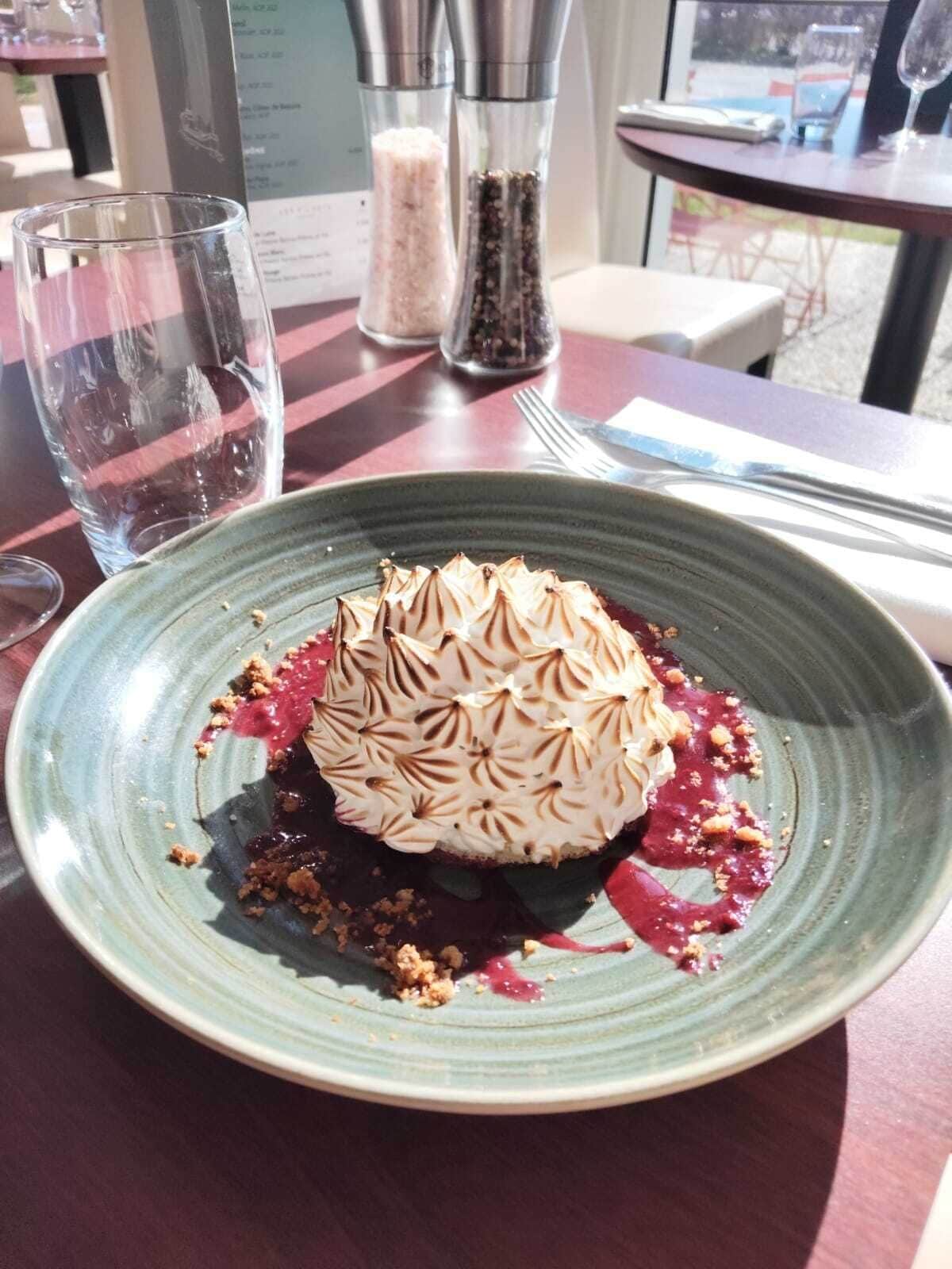 Ein Dessert auf einem Teller mit gemustertem Belag, dazu ein Glas und Salz- und Pfefferstreuer auf einem Tisch.