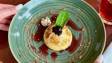 A dessert on a green plate with a mint leaf, held by a person with white nail polish.