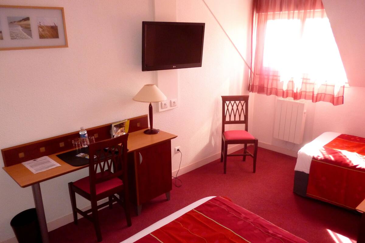 Een hotelkamer met een bureau, stoel, bed, televisie en raam met gordijnen.