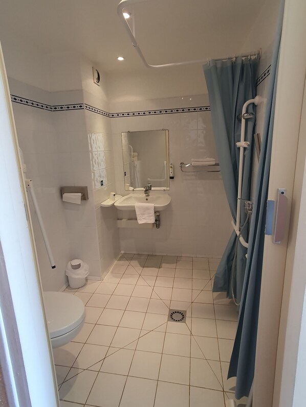 Une salle de bain comprenant des toilettes, un lavabo, un miroir, un rideau de douche et un sol carrelé.