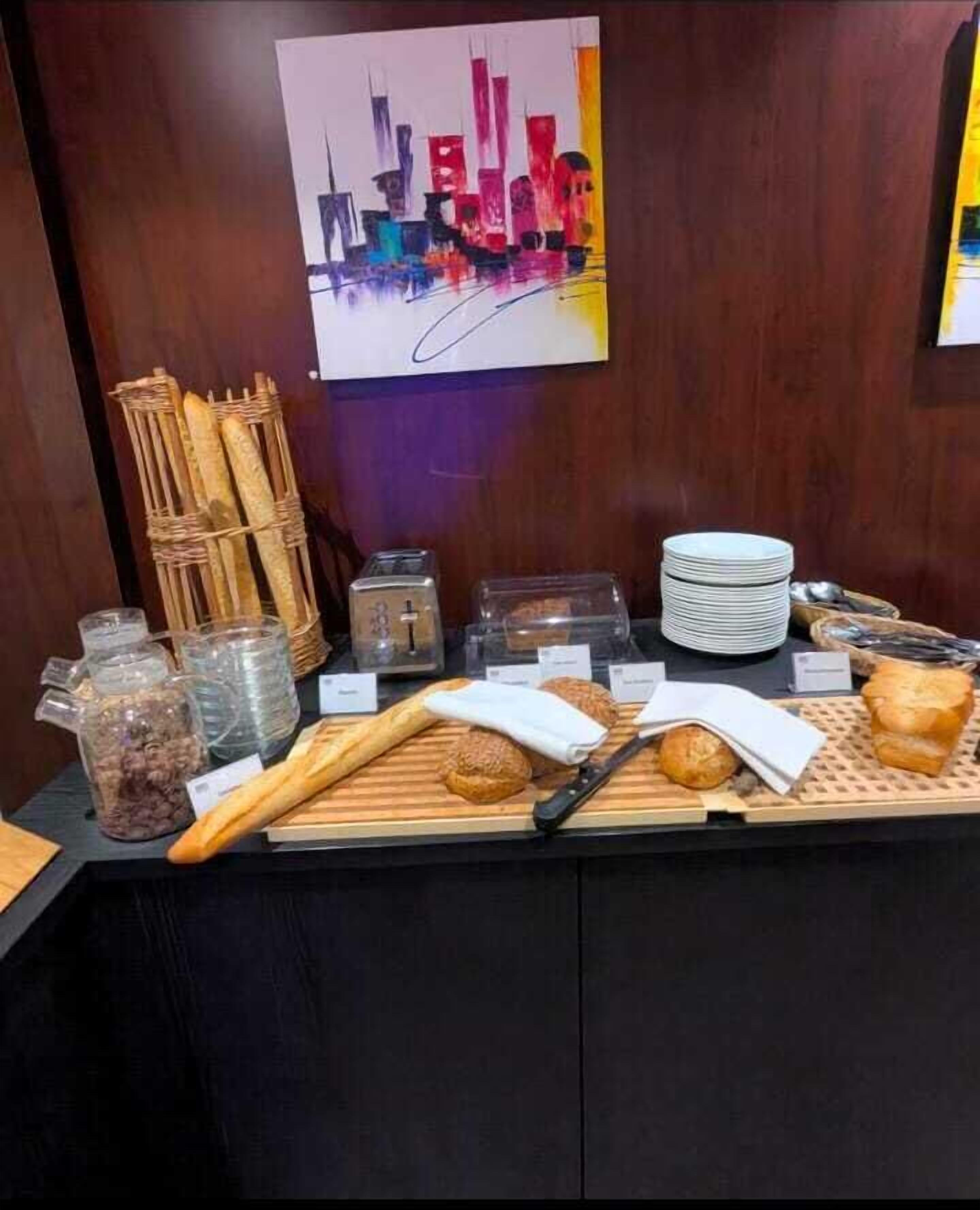 Un bufé de desayuno con baguettes, panecillos, un cuchillo y varios recipientes.