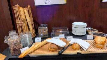 Un bufé de desayuno con baguettes, panecillos, un cuchillo y varios recipientes.