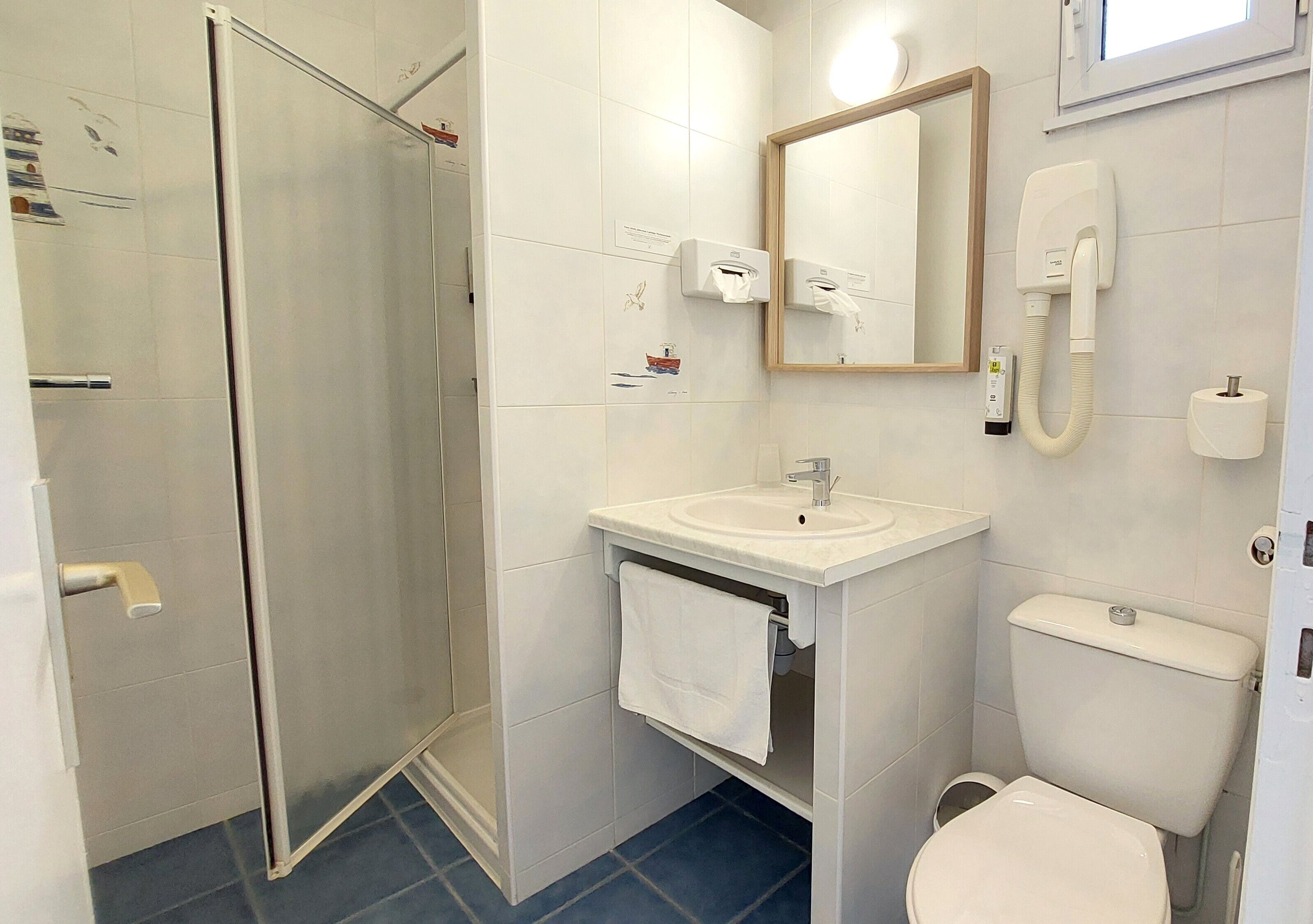 Un baño con cabina de ducha de vidrio, lavamanos con toalla, inodoro y espejo.
