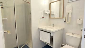 Un baño con cabina de ducha de vidrio, lavamanos con toalla, inodoro y espejo.
