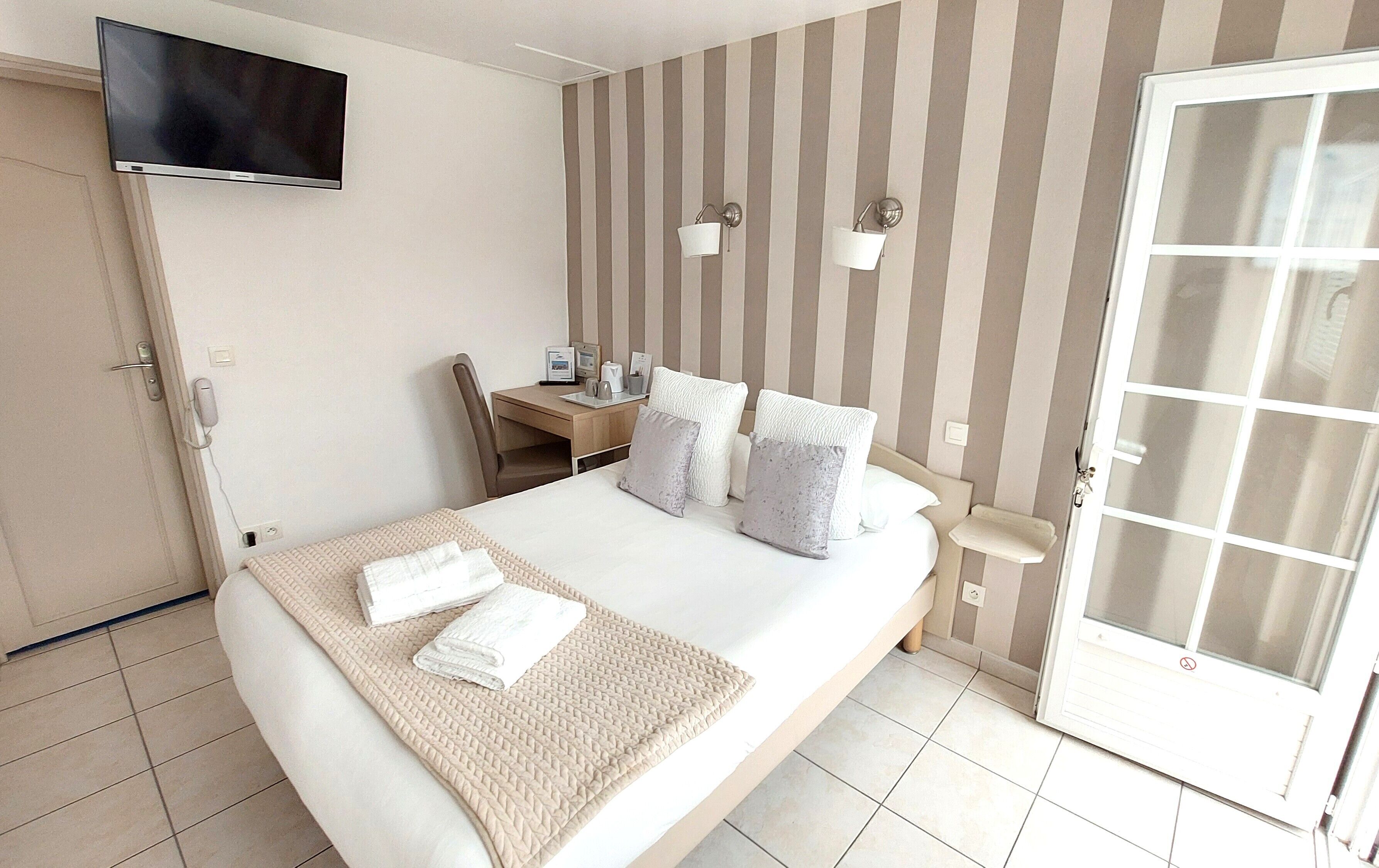 A hotel room with a bed, bedside table, lamp, and a TV mounted on the wall.