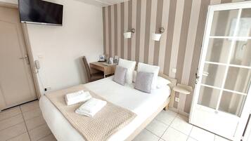 A hotel room with a bed, bedside table, lamp, and a TV mounted on the wall.