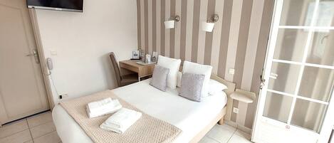 Een hotelkamer met een bed, nachtkastje, lamp en een aan de muur bevestigde televisie.