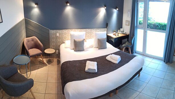 Quarto de hotel com uma cama grande, uma mesinha redonda, uma cadeira, uma escrivaninha com cadeira e vista para o exterior por uma porta de correr.