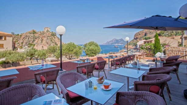 An outdoor dining area with wicker chairs and tables, overlooking a coastal landscape with a view of the sea and hills. - Hotel Kalliste (Ota)