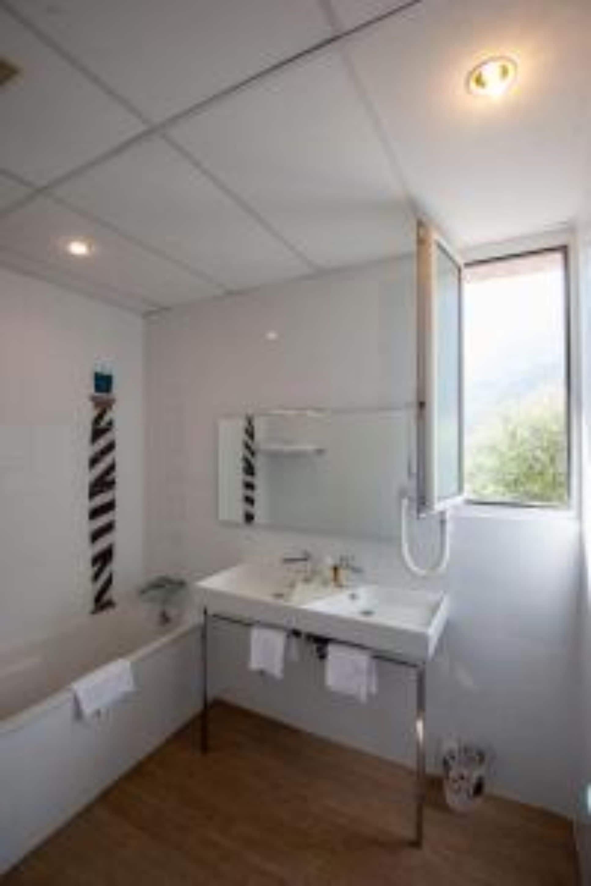 Un baño moderno con tocador blanco, un espejo grande, ducha y ventana que proporciona luz natural.