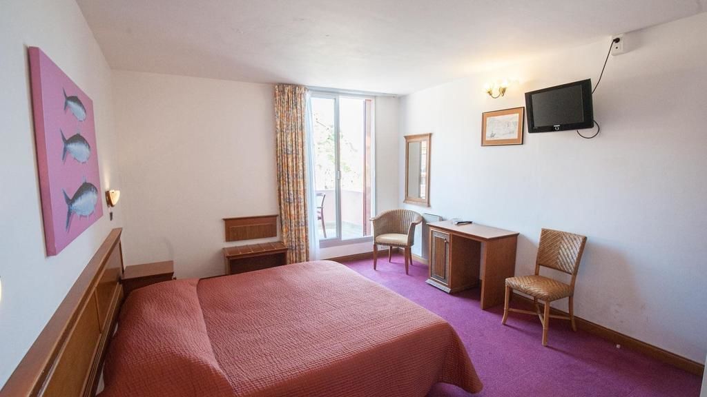 A hotel room with a bed, a desk, a chair, a television, and a window with curtains.